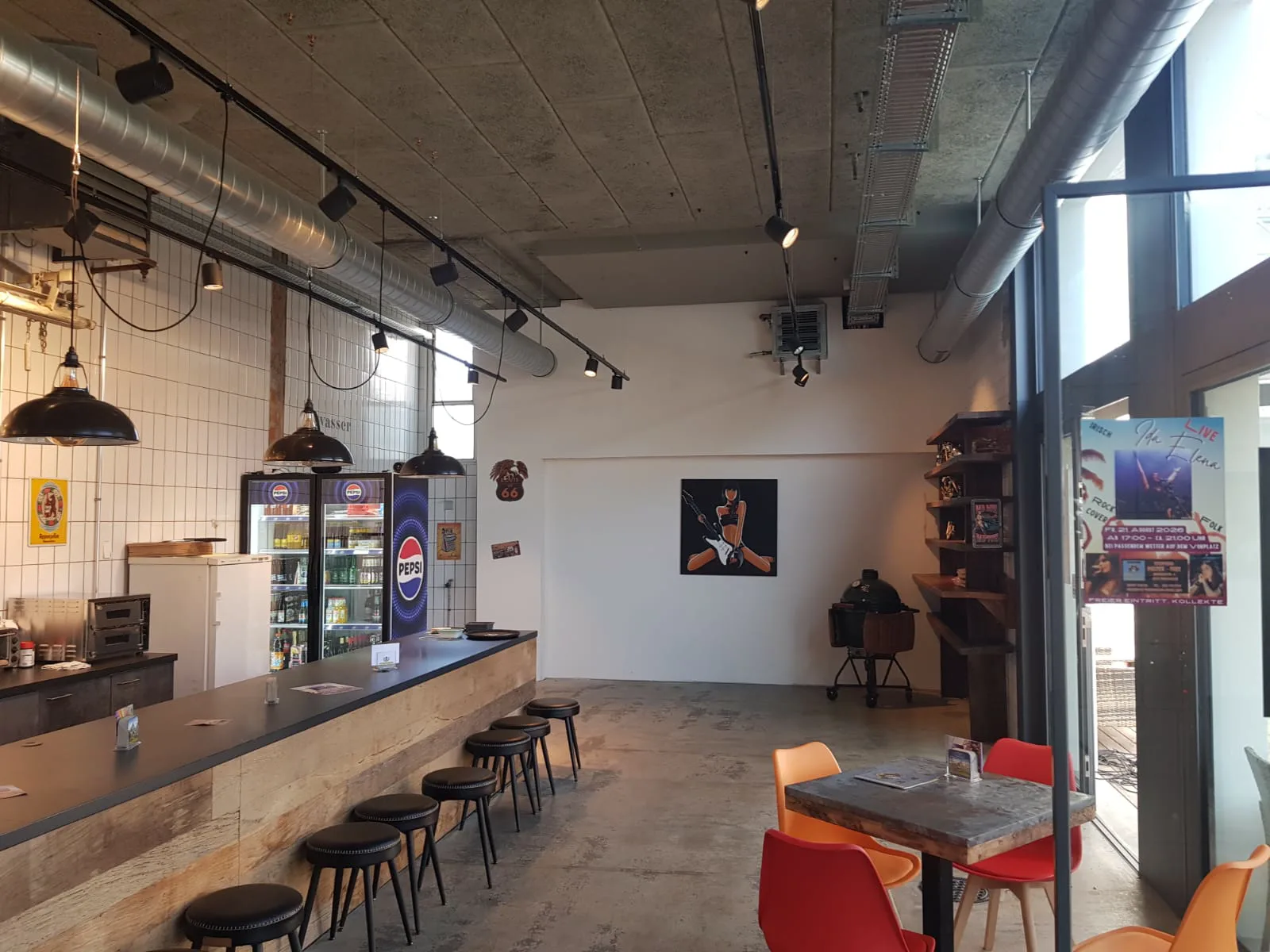 Die Bar mit dem Getränkekühlschrank; dahinter öffnet sich der Raum zu einer freien Fläche mit einem Kugelgrill.