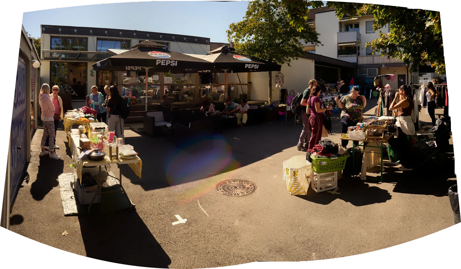 Panorama über den Platz vor dem Pulfer-fass: Pepsi-Schirme, Stände mit Kleidern und Kisten, Leute in der Sonne.