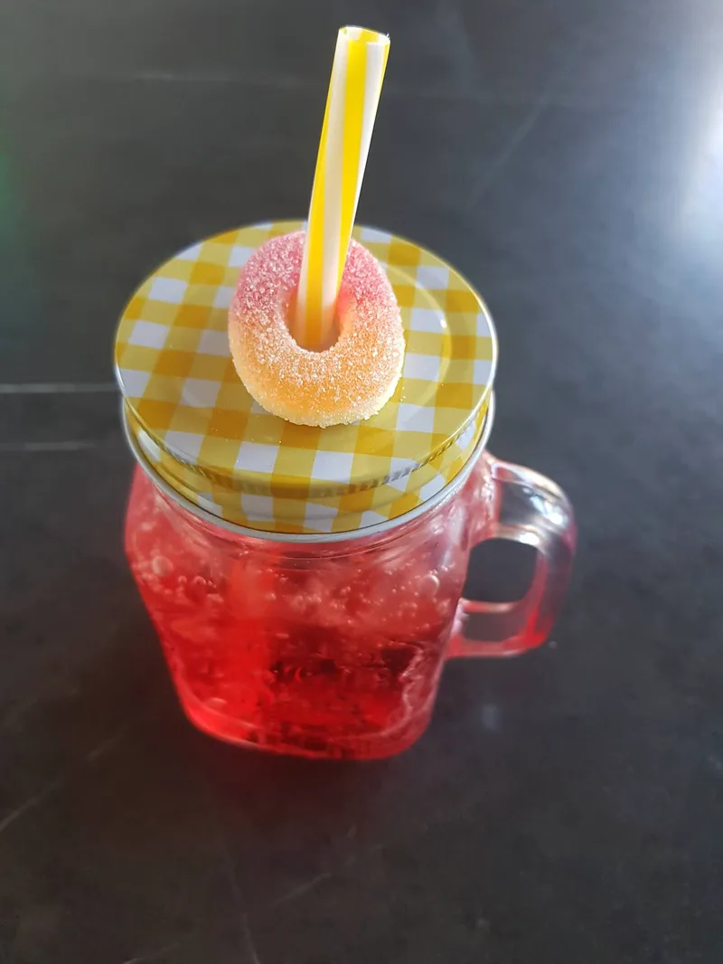 Ein rot-oranger Mixdrink mit Eis in einem Bügelglas, mit Strohhalm.