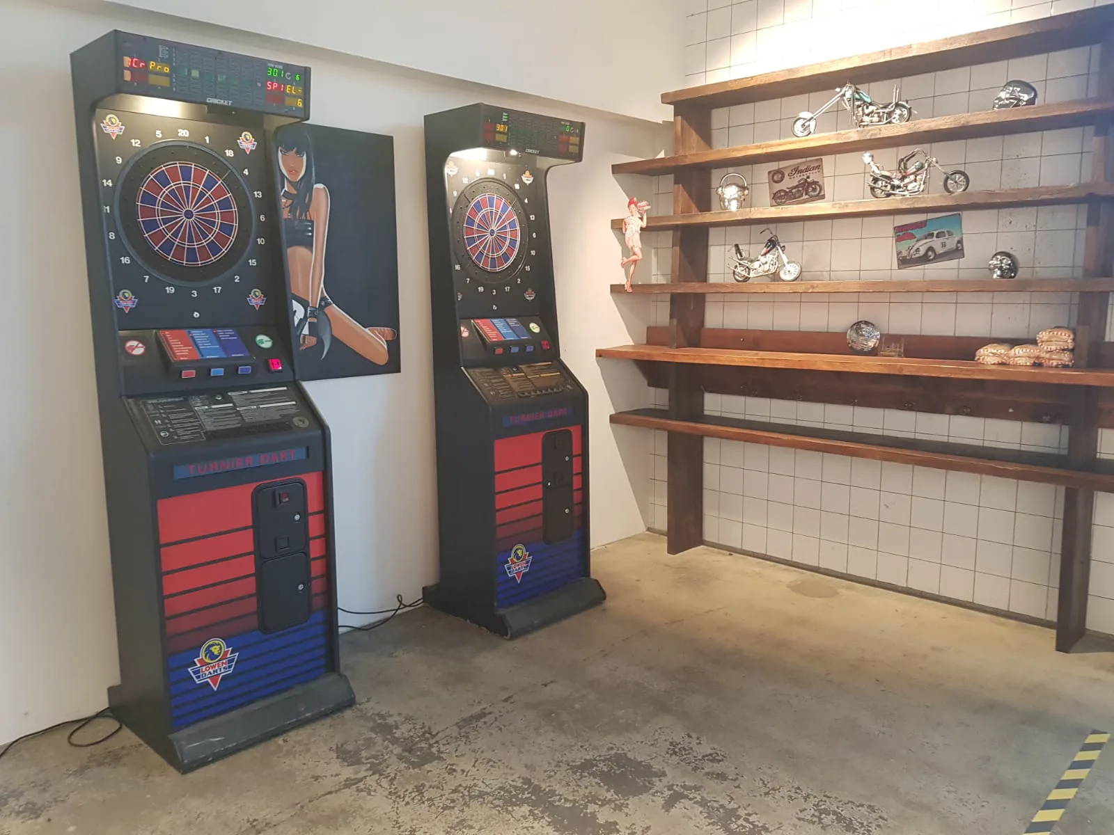 Der hintere Raum: an der Wand zwei Dartautomaten, daneben ein hohes Holzregal mit Modellmotorrädern und Blechschildern.