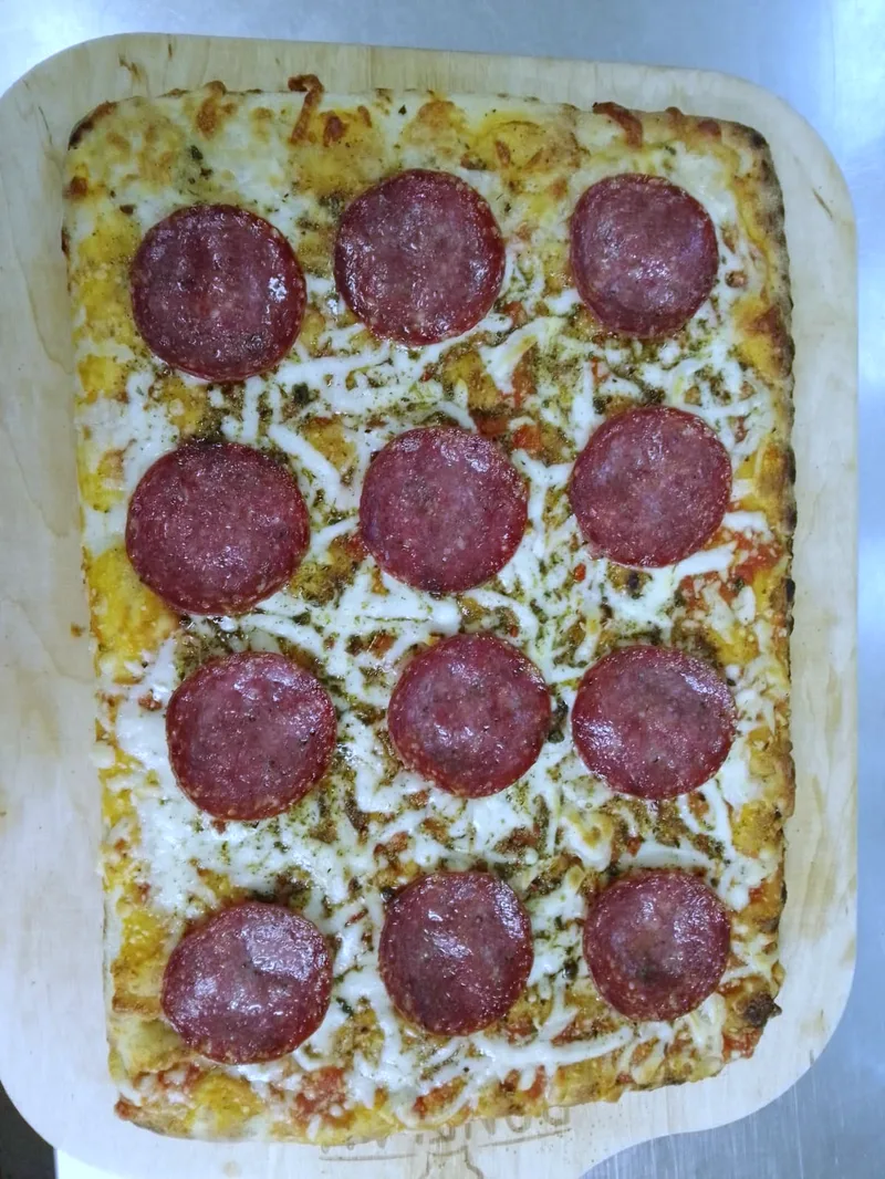 Eine rechteckige Pizza mit Salami auf einem Holzbrett.