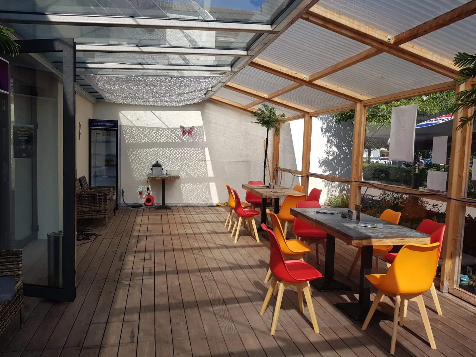 Dieselbe Terrasse bei Sonnenschein, das Licht fällt durch das Dach auf die Holzdielen.
